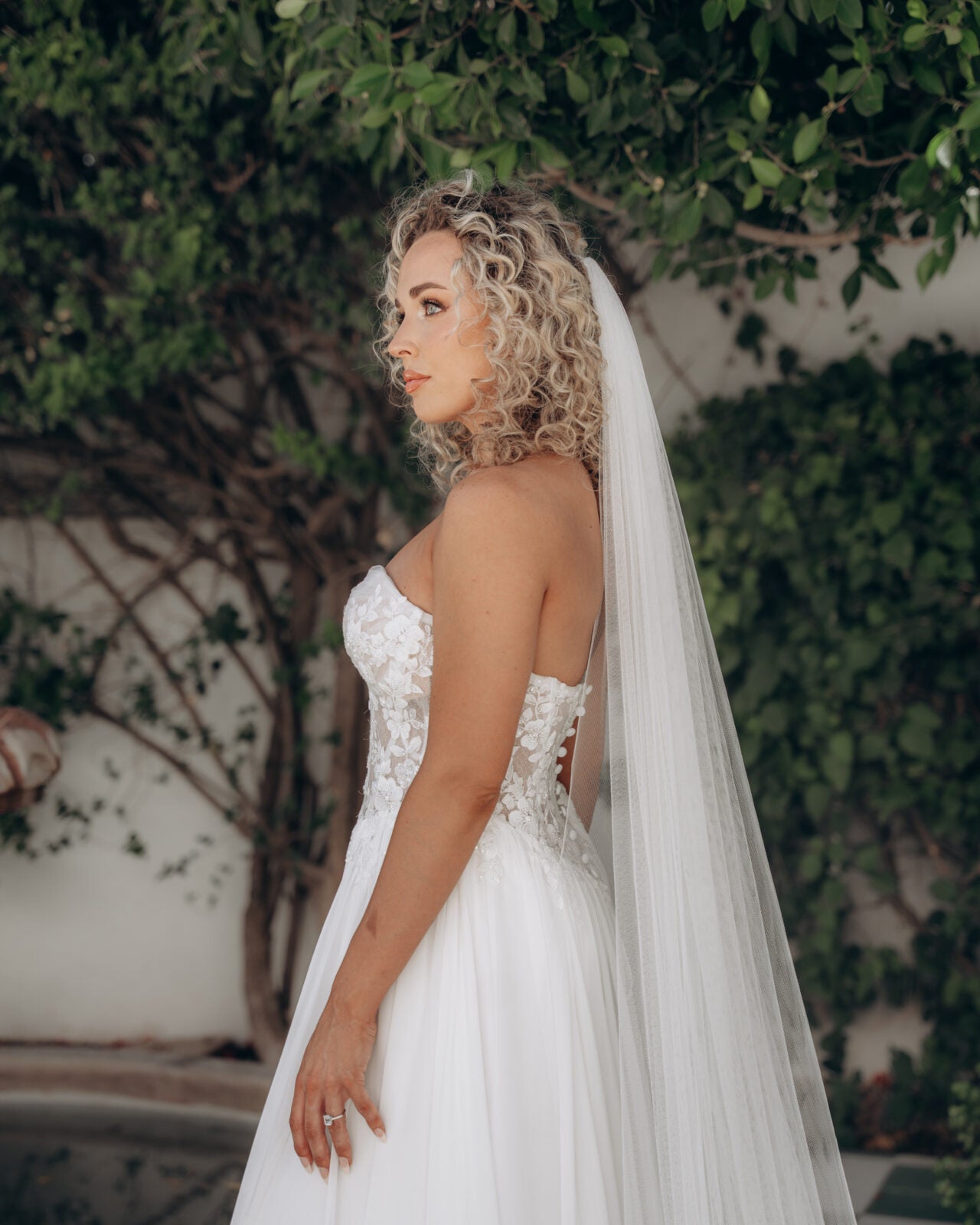 Bride in a white ivory strapless wedding dress with sweetheart neckline and a veil standing outdoors.