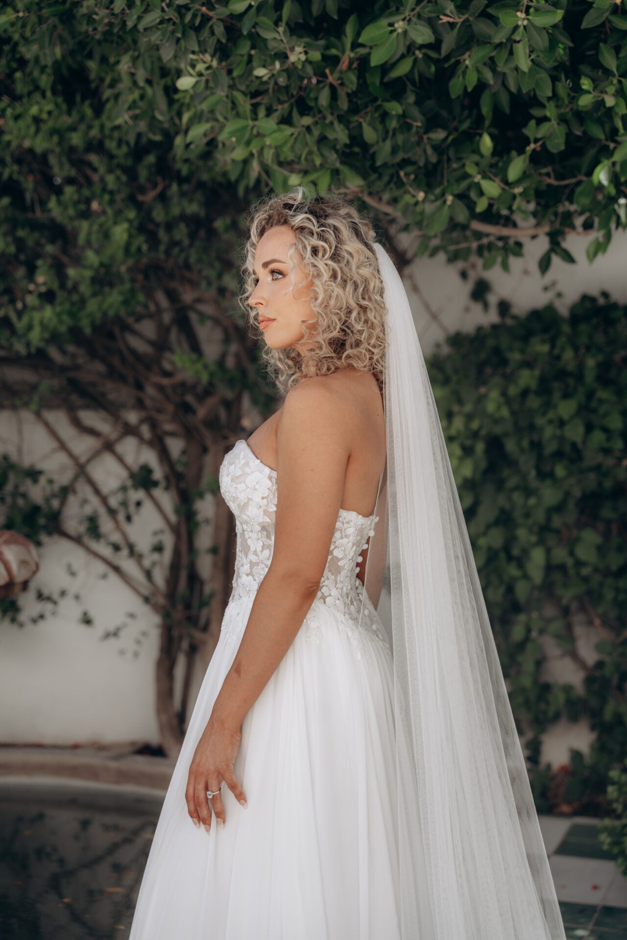 Bride in a white ivory strapless wedding dress with sweetheart neckline and a veil standing outdoors.