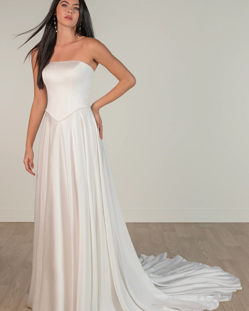 Bride wearing a strapless white ivory satin wedding dress with a flowing train, strapless neckline and boned corset.