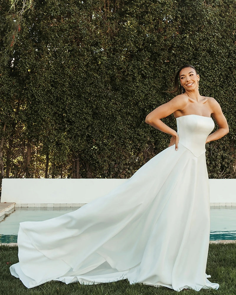 Bride in a white ivory chiffon strapless gown standing outdoors with greenery in the background.