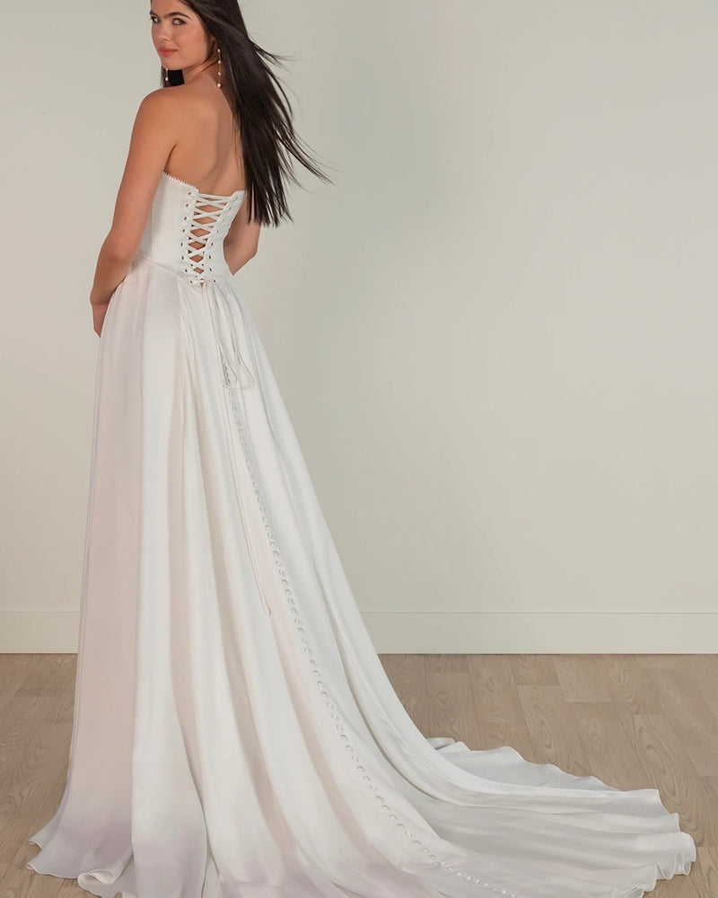 Woman wearing a white wedding dress with a flowing skirt on a plain background