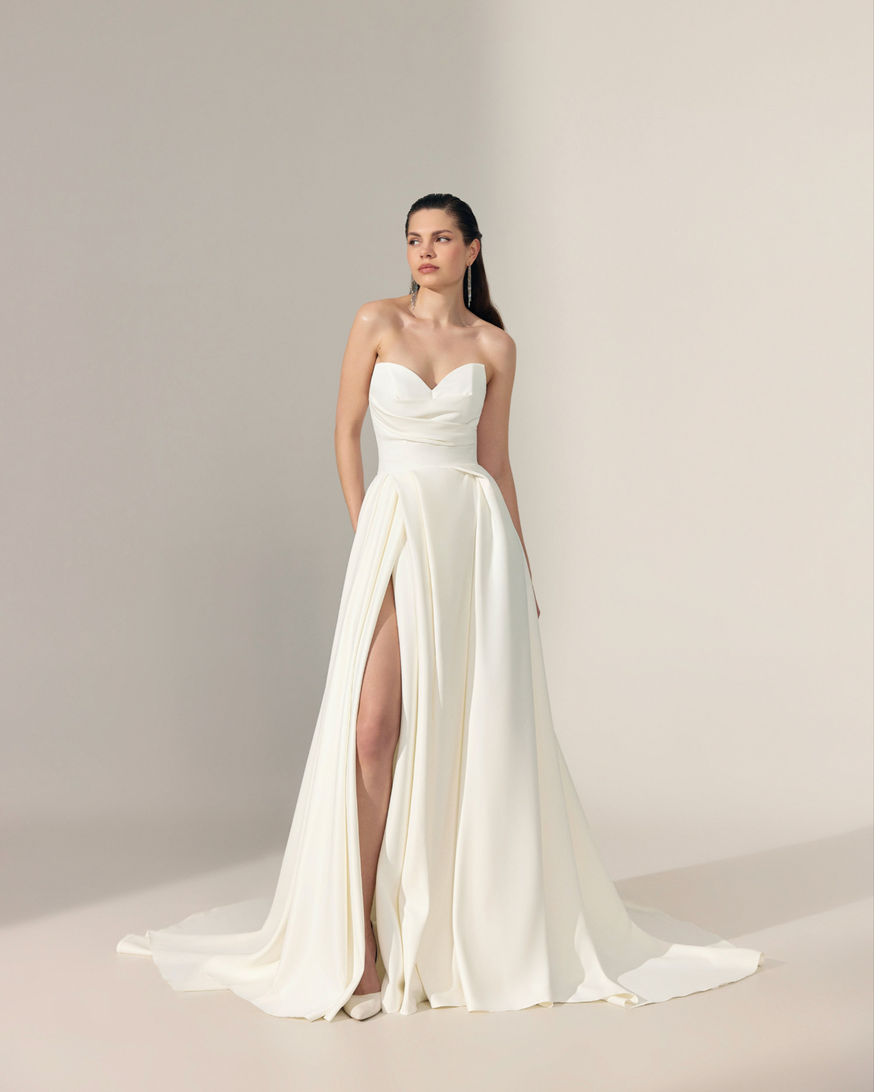 A bride in a strapless white ivory wedding gown with a sweetheart neckline, fitted bodice, high front slit, and a long flowing train.