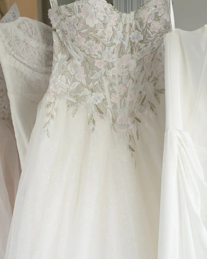 White wedding dress with floral lace details hanging on a rack.