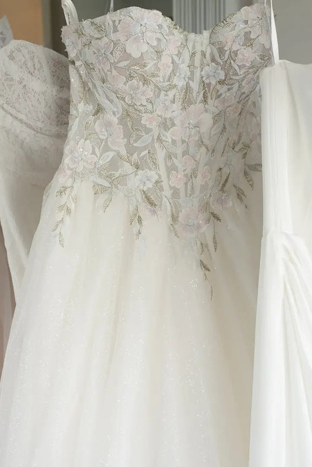 White wedding dress with floral lace details hanging on a rack.