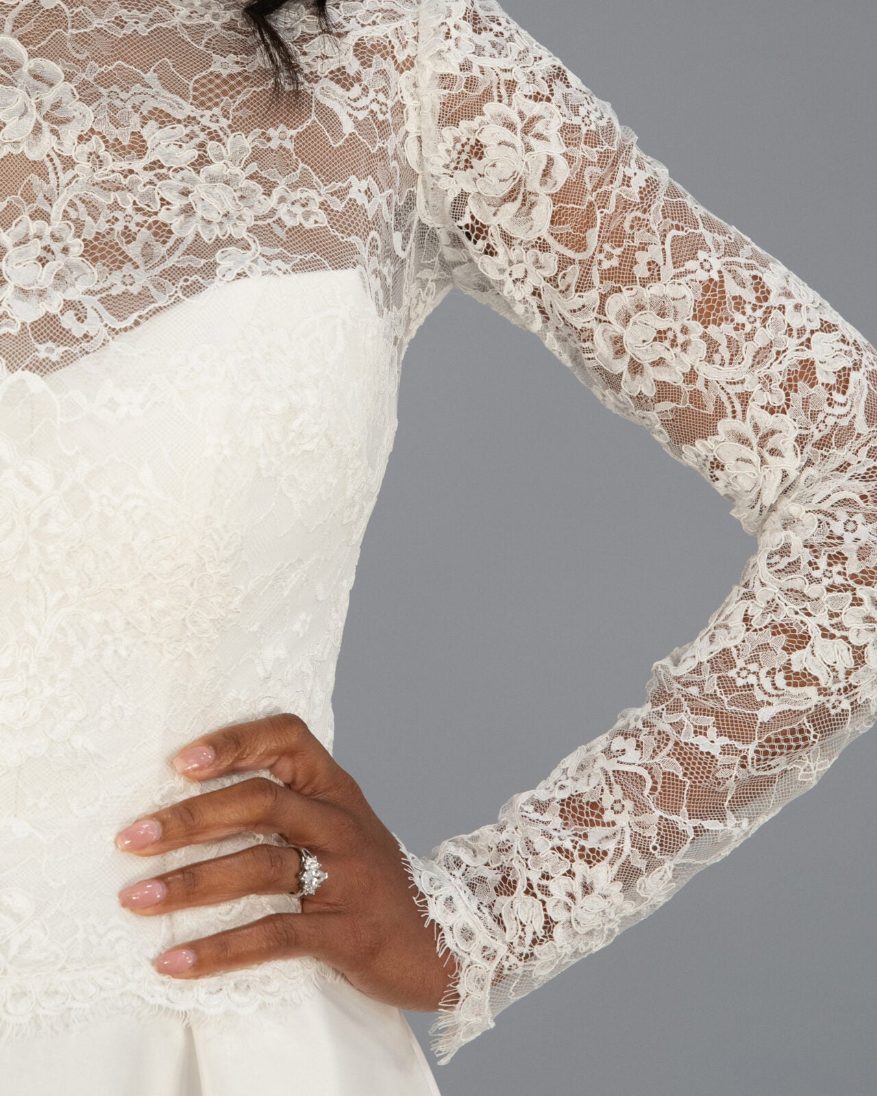 A close-up of a white ivory lace long-sleeve bridal jacket with satin wedding dress with sheer floral lace sleeves and a smooth white bodice.