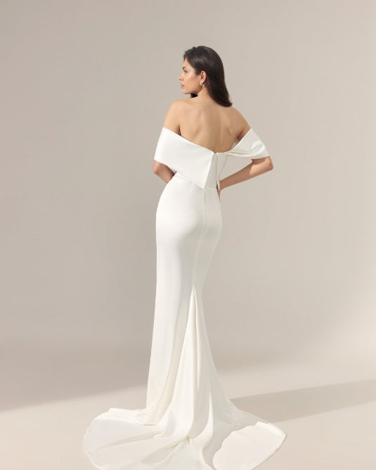 A off-the-shoulder wedding gown from the back, featuring a dramatic off shoulder detail at the back of the neckline and a long flowing train.
