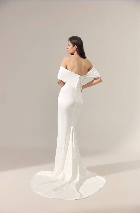 A off-the-shoulder wedding gown from the back, featuring a dramatic off shoulder detail at the back of the neckline and a long flowing train.