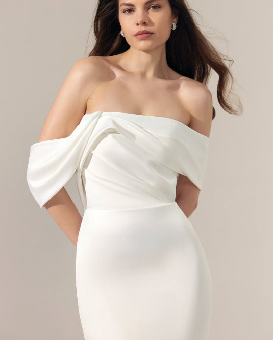 Off-the-shoulder ivory satin wedding dress with a draped, gathered bodice and a fitted skirt.