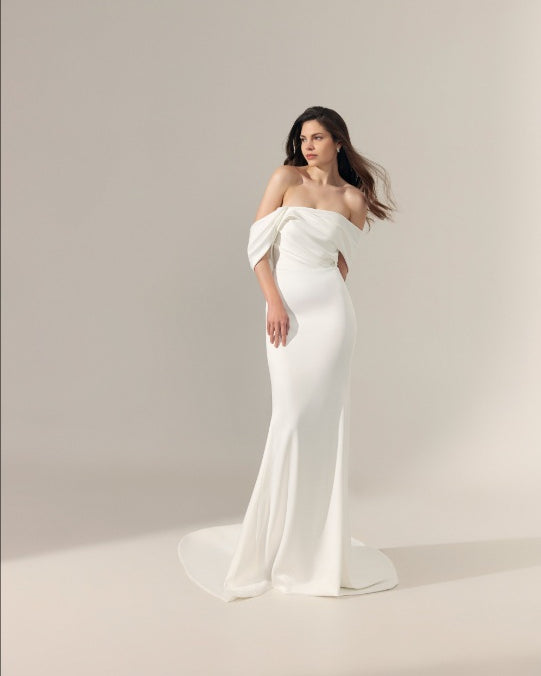Off-the-shoulder floor-length ivory wedding gown with a fitted silhouette and a slight train.
