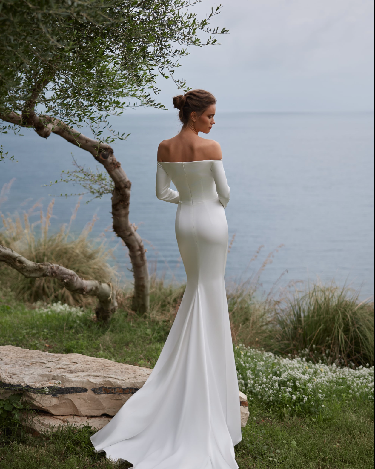 A woman wearing an off-the-shoulder white wedding gown with long sleeves and small train.