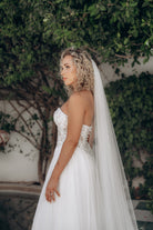 Bride in a white ivory strapless wedding dress with sweetheart neckline and a veil standing outdoors.