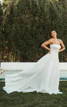 Bride in a white ivory chiffon strapless gown standing outdoors with greenery in the background.
