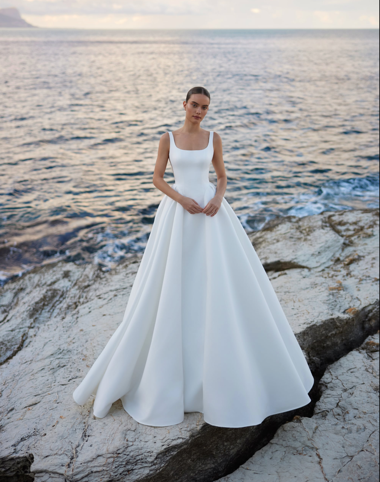 A bride wearing an A-line ivory wedding gown with straps and square neckline.