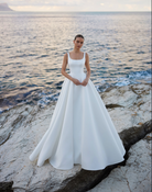 A bride wearing an A-line ivory wedding gown with straps and square neckline.