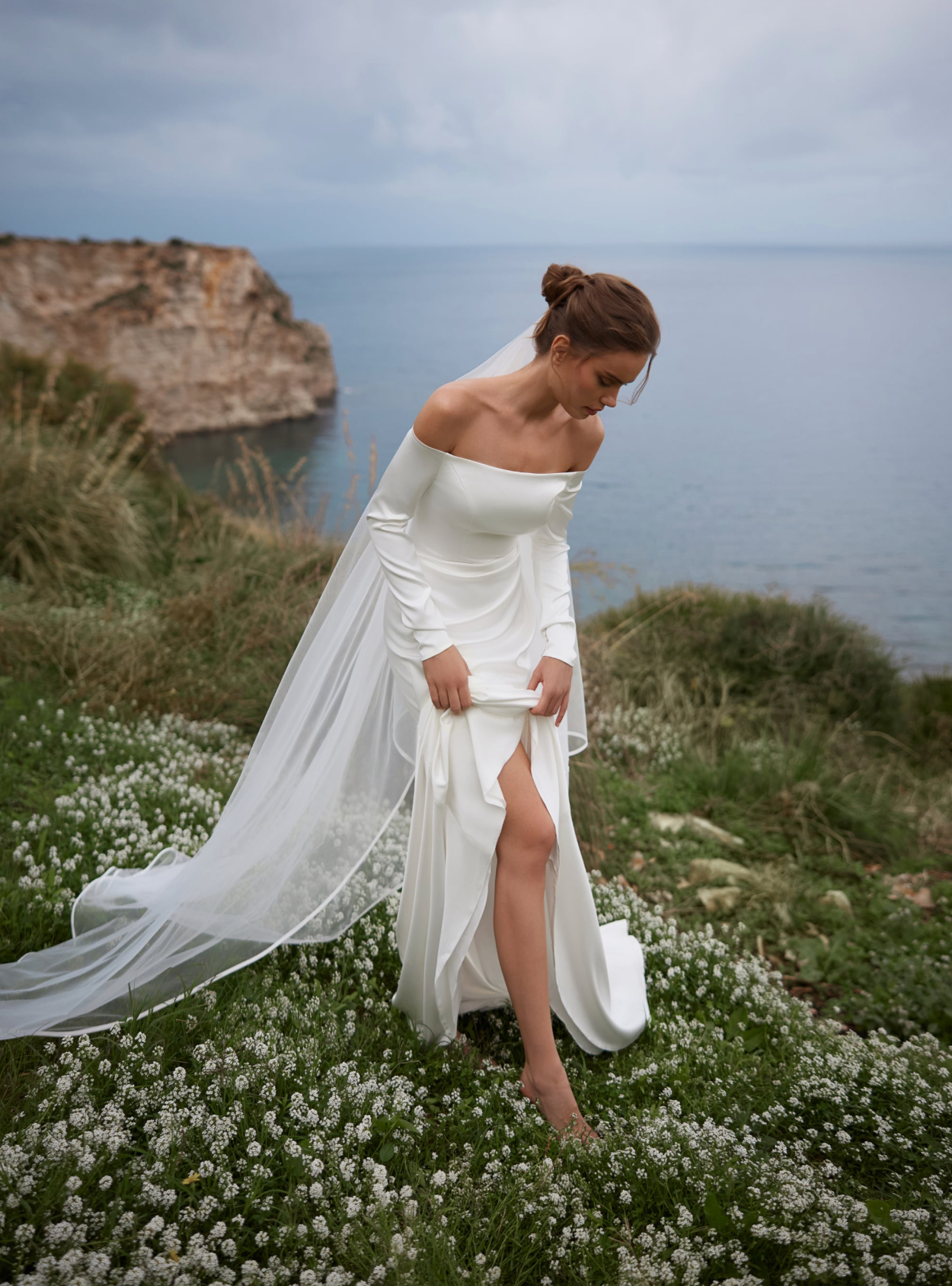 A bride in a white off-the-shoulder wedding dress with sleeves and a long sheer veil.