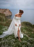 A bride in a white off-the-shoulder wedding dress with sleeves and a long sheer veil.