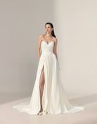 A bride in a strapless white ivory wedding gown with a sweetheart neckline, fitted bodice, high front slit, and a long flowing train.