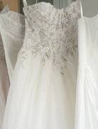 White wedding dress with floral lace details hanging on a rack.