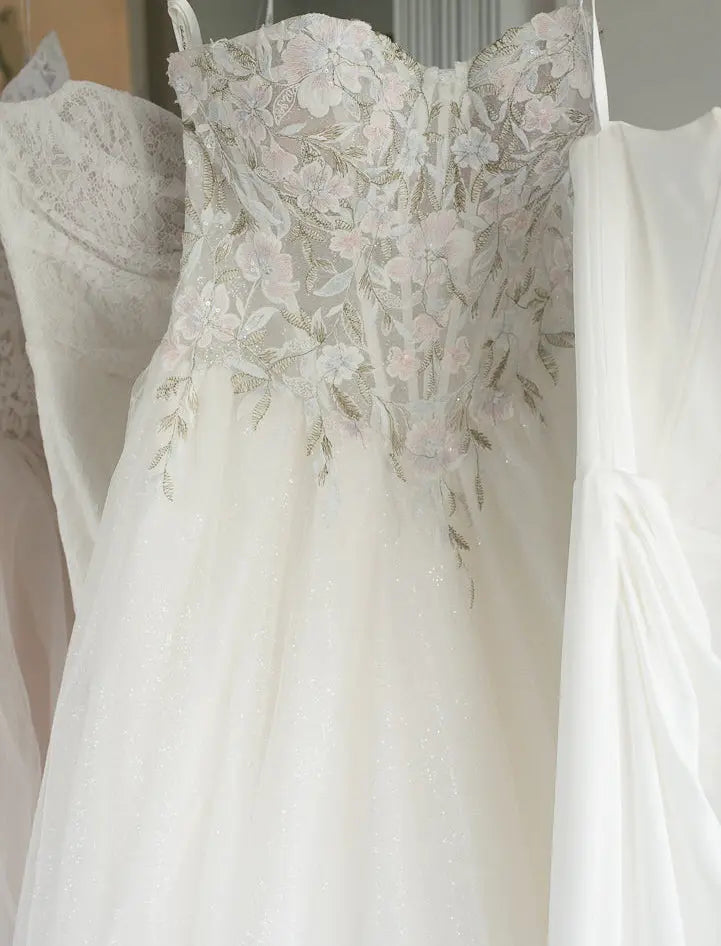 White wedding dress with floral lace details hanging on a rack.