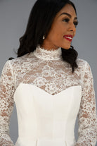 A bride wearing a white ivory lace mock-neck long-sleeve bridal jacket with a structured white corset-style bodice.