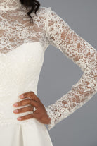 A close-up of a white ivory lace long-sleeve bridal jacket with satin wedding dress with sheer floral lace sleeves and a smooth white bodice.