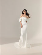 Off-the-shoulder floor-length ivory wedding gown with a fitted silhouette and a slight train.