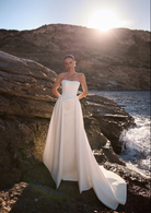 A woman wearing a strapless white ivory wedding gown with rouching and overskirt.