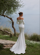 A woman wearing an off-the-shoulder white wedding gown with long sleeves and small train.