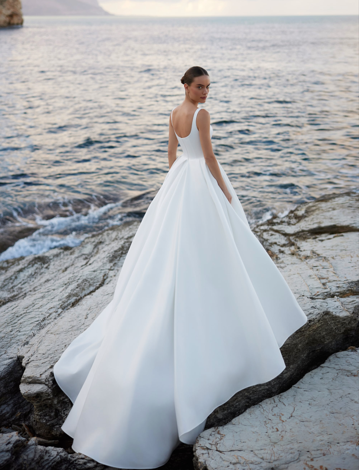 A woman wearing a white ivory a-line wedding gown with straps and full skirt.